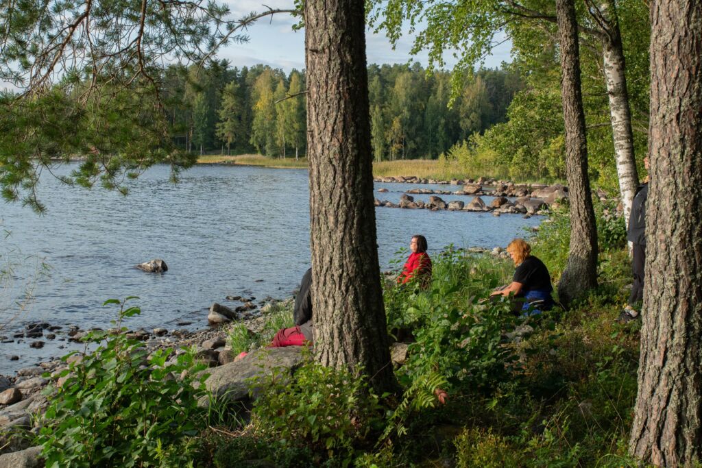 Kolme henkilöä istuu järven rannalla.