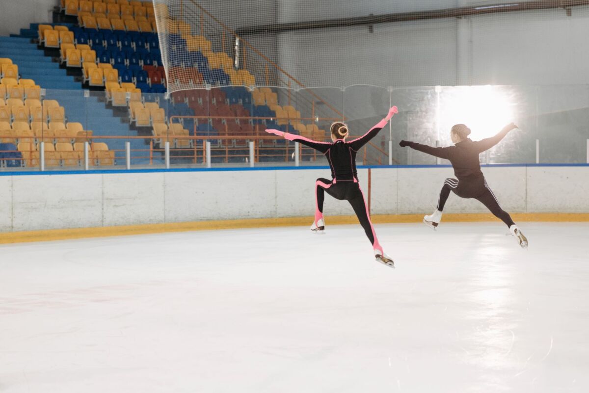 Kaksi taitoluistelijaa tekee hypyn jäähallissa