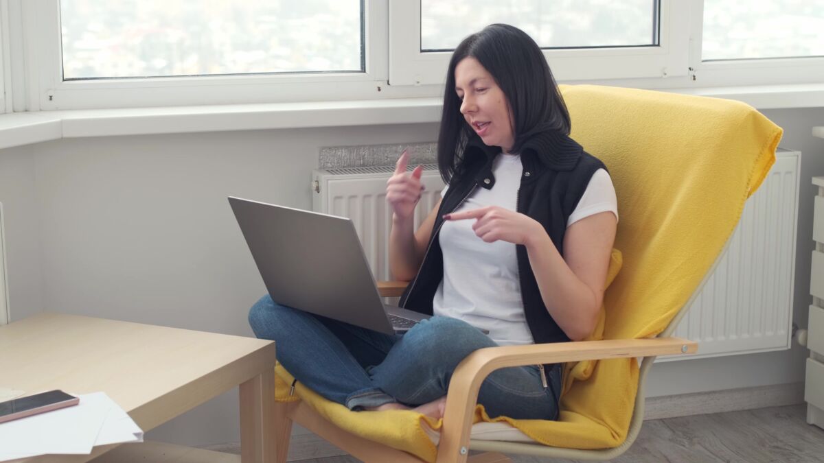 Nainen istuu keltaisessa nojatuolissa, sylissään tietokone.