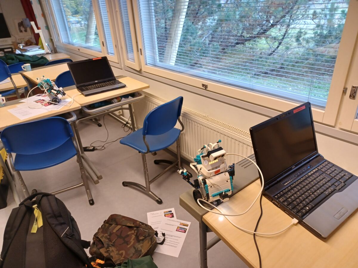 Koululuokka jossa pulpettien päällä tietokoneet ja legorobotti