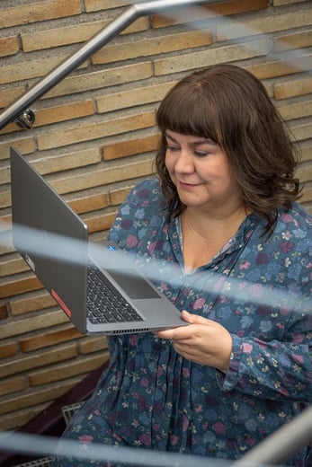Nainen tietokone kädessään, taustalla tiiliseinä