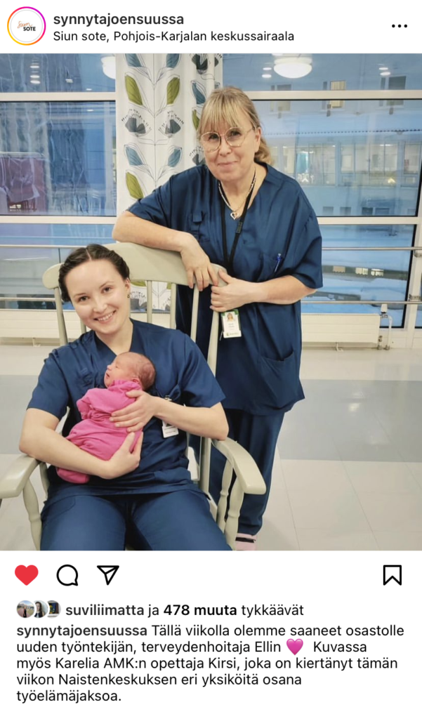 Kaksi sairaanhoitajaa, toinen istuu tuolissa vastasyntynt vauva sylissä, toinen seisoo vieressä.