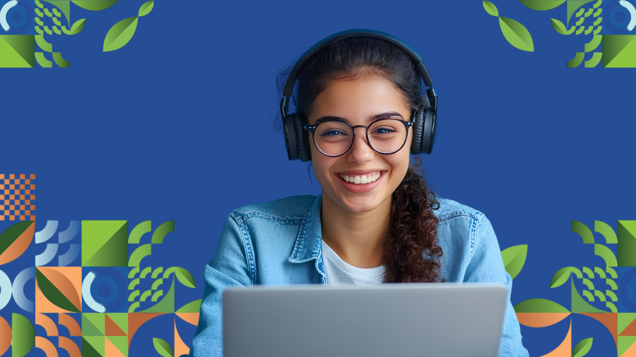 A smiling student sits in front of a computer, wearing headphones.