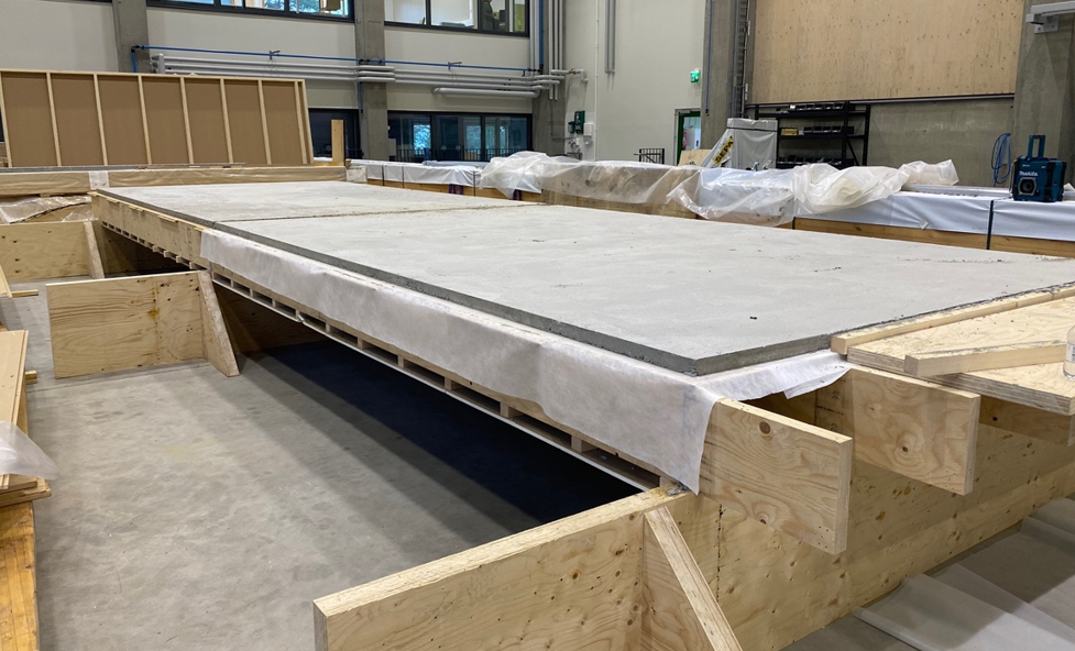 Teollisuushalli, jossa suuria rakennuksen välipohjarakenteita. Rakennelman alaosa on liimapuuta ja päällimmäisenä on betonilevy.