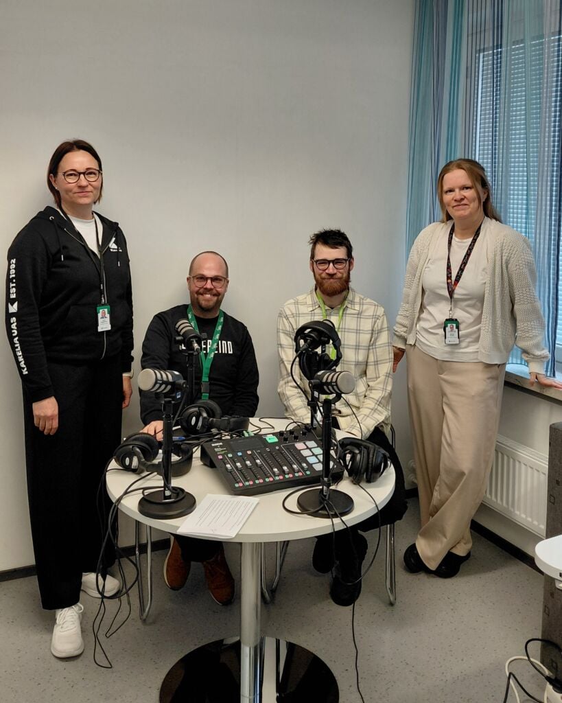Four people gathered around a table with podcast equipment: microphones etc.