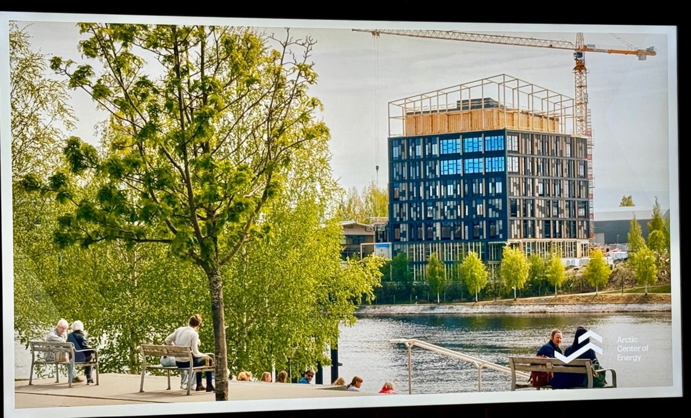 Kaupunkimaisema jossa taustalla rakennusvaiheessa oleva puukerrostalo ja nosturi. Rakennuksen edessä vesistö. Vesistön rannalla ihmisiä istumassa penkeillä.