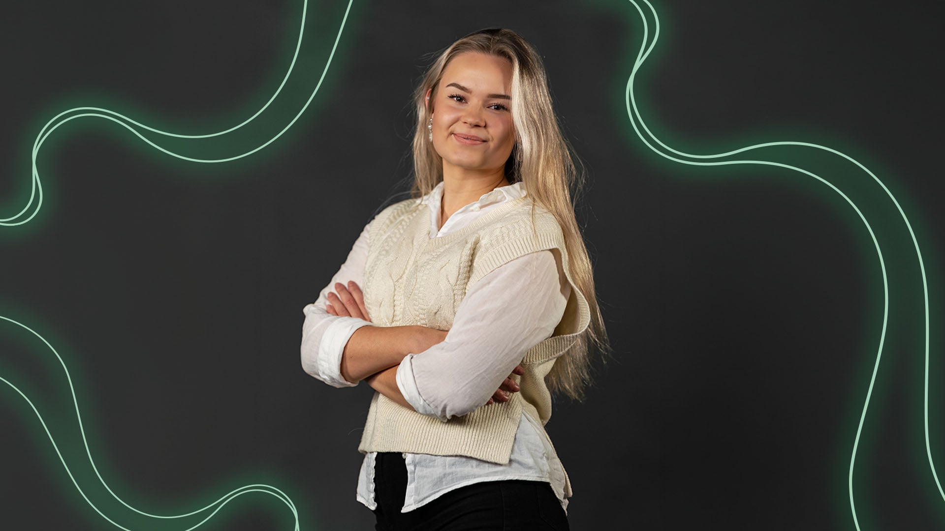 Muotokuva henkilöstä, joka seisoo käsivarret ristissä vaaleassa neuleliivissä ja valkoisessa paidassa. Taustalla on tumma, mustanharmaa pinta, jonka päällä kulkee vihreitä, aaltoilevia valoviivoja. Henkilö katsoo suoraan kameraan.